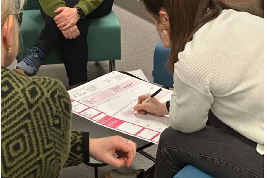 En gruppe mennesker som sitter ved et bord og fyller ut et skjema