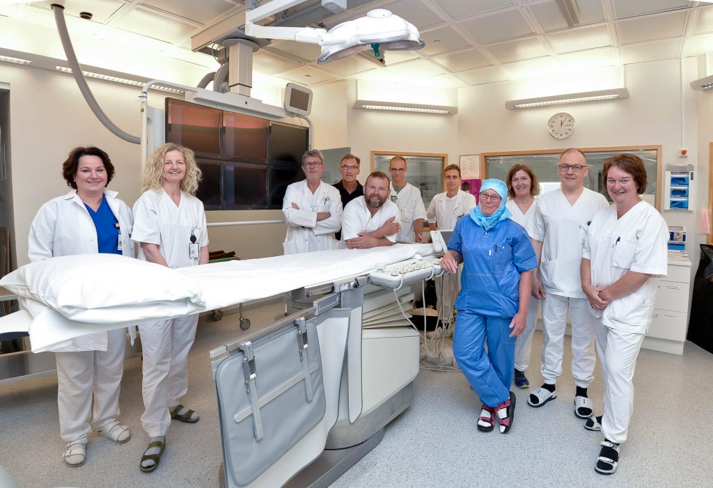 En gruppe mennesker i hvite laboratoriefrakker står ved siden av en stor hvit maskin