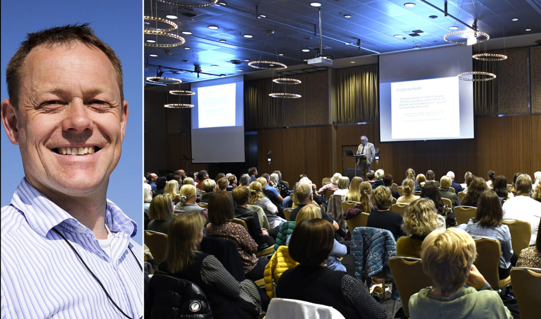 En mann som smiler foran en gruppe mennesker i et rom