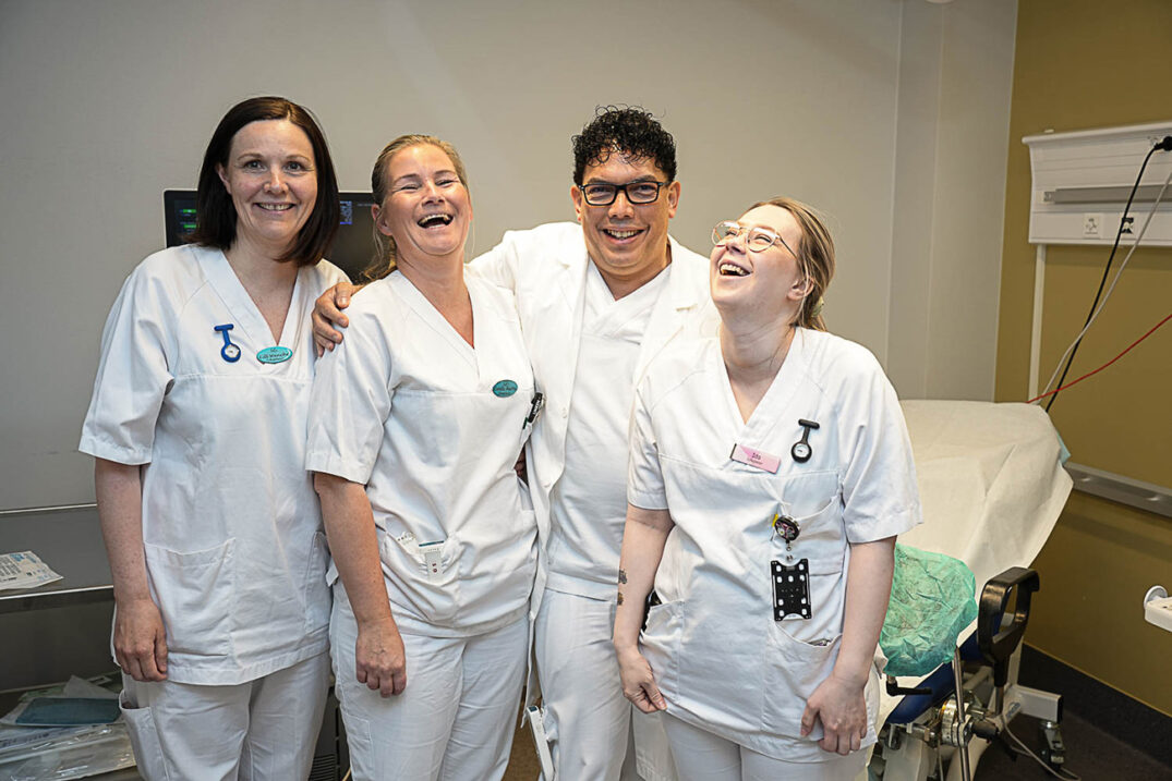 Tre damer og en mann i hvitt på pasientrom