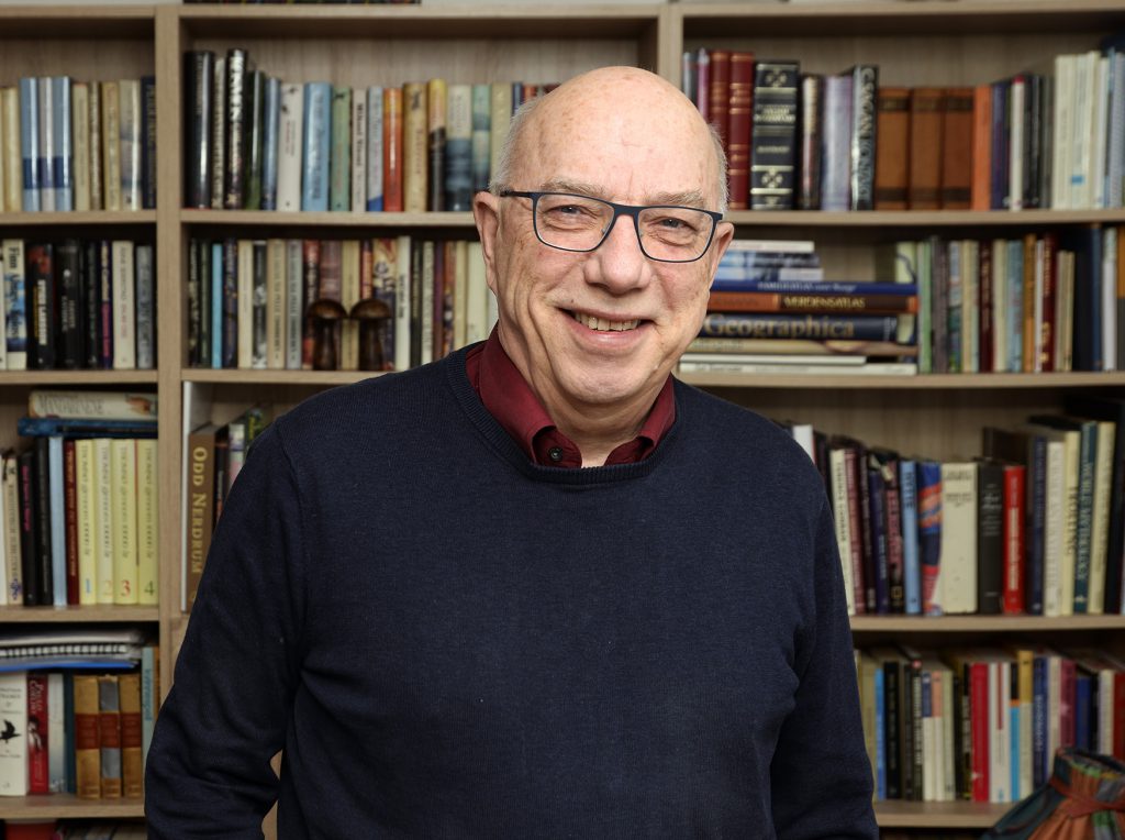 En mann som smiler foran en bokhylle