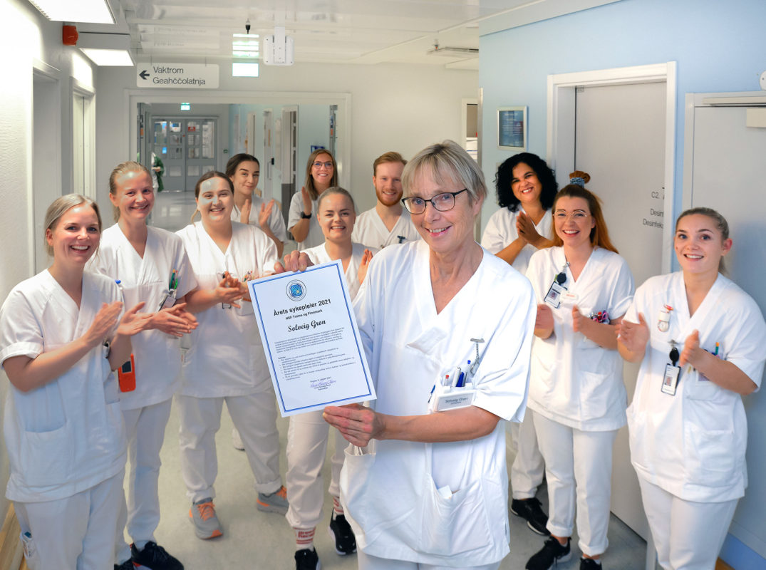 En gruppe mennesker iført hvite laboratoriefrakker som holder et skilt