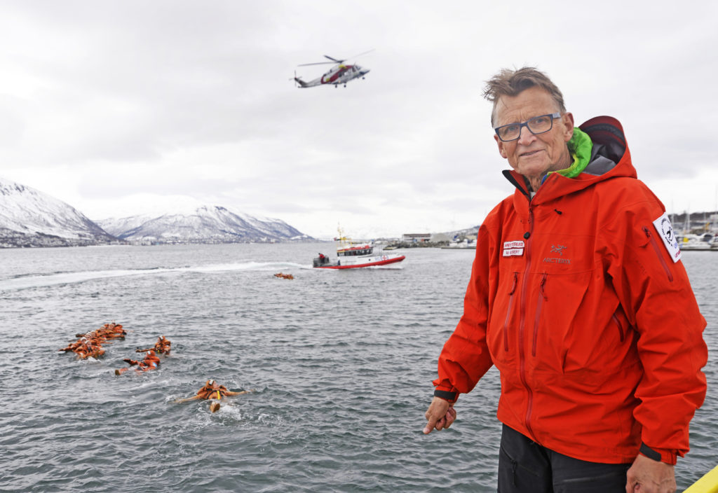 En mann som står foran et vannområde med et helikopter flyvende over seg