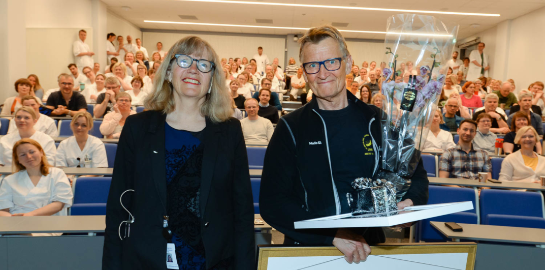 En mann og en kvinne står ved en talerstol med en folkemengde bak seg