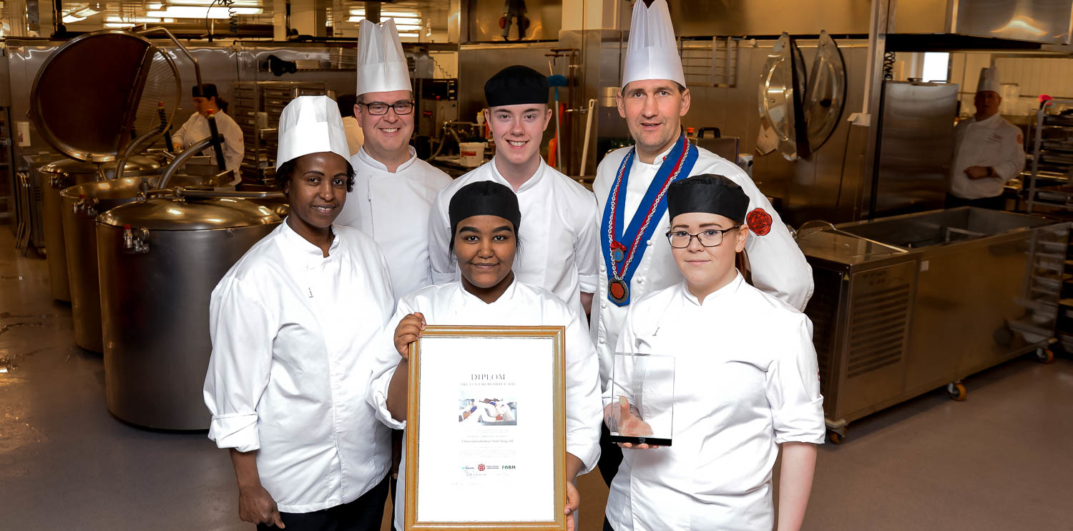 En gruppe mennesker iført hvite uniformer og med et sertifikat