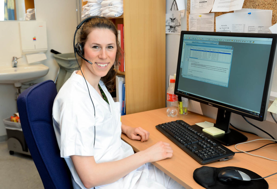 En person med headset og sittende ved et skrivebord med en datamaskin