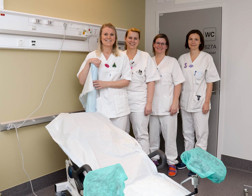 En gruppe kvinner i hvite laboratoriefrakker står ved siden av en pasient