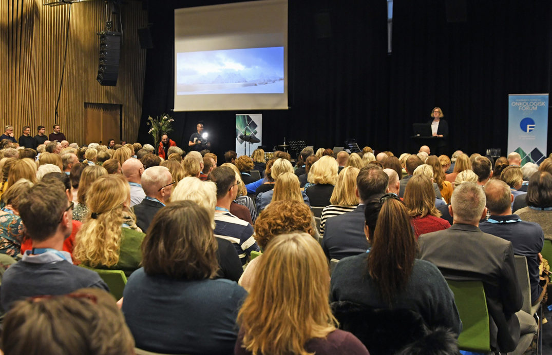 En gruppe mennesker som sitter i et rom og ser på en person på en scene