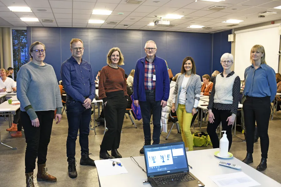 En gruppe mennesker som står i et rom med en bærbar PC