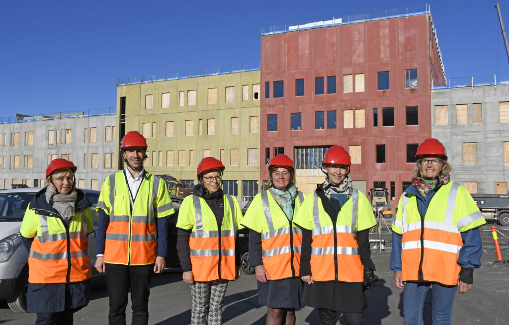 En gruppe menn i oransje vester står foran en bygning