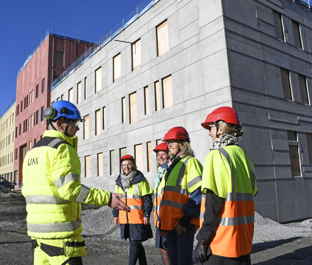 En gruppe menn i sikkerhetsvester står utenfor en bygning