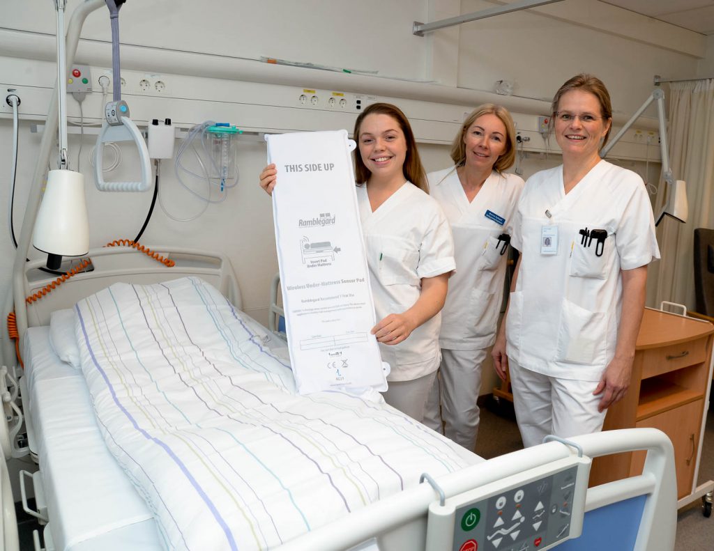 En gruppe kvinner i hvite frakker står ved siden av en sykehusseng