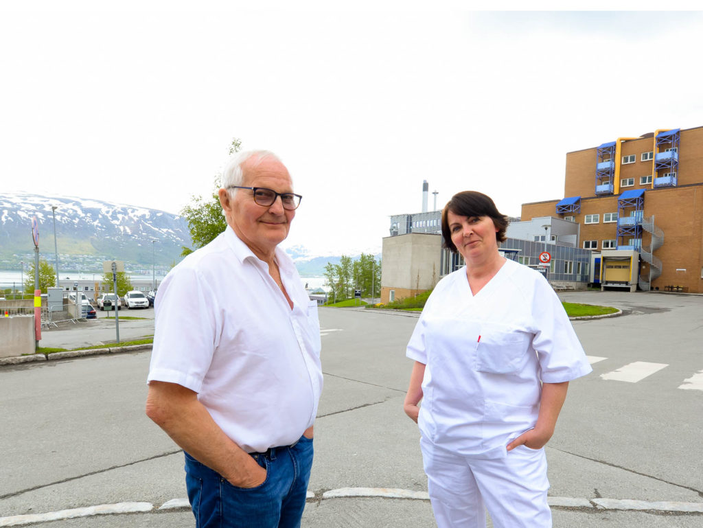 En mann og en kvinne står på en parkeringsplass med bygninger i bakgrunnen