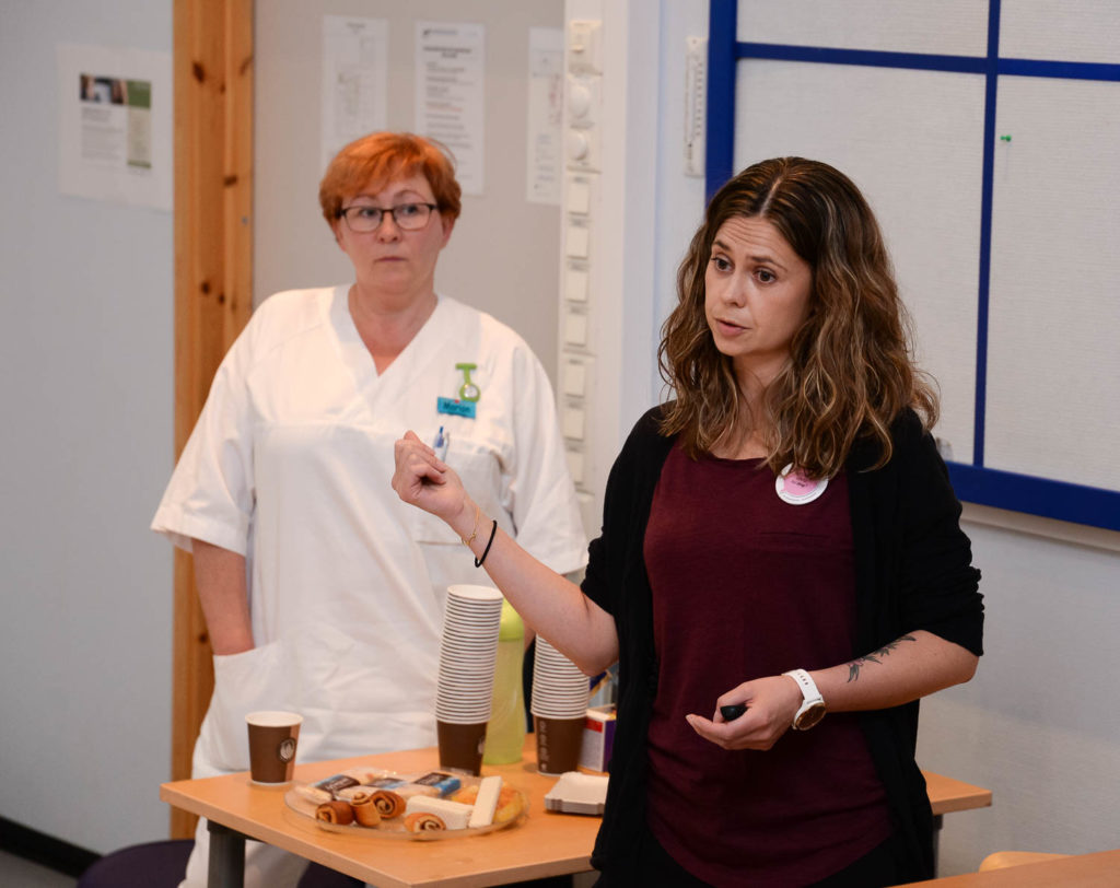 En kvinne og en mann står i et rom med et bord og en whiteboard