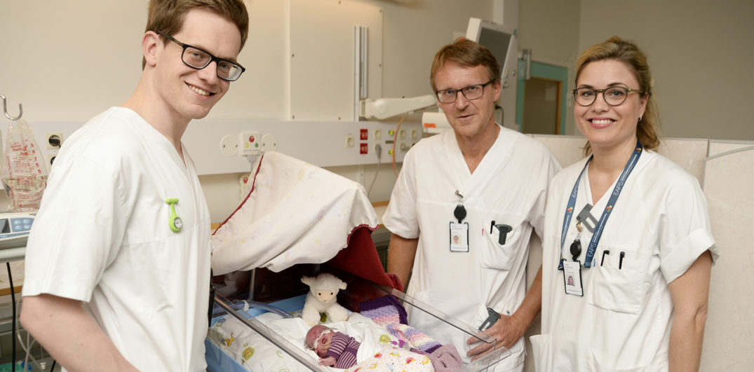 En gruppe mennesker i hvite skjorter som står ved siden av en baby i en sykehusseng