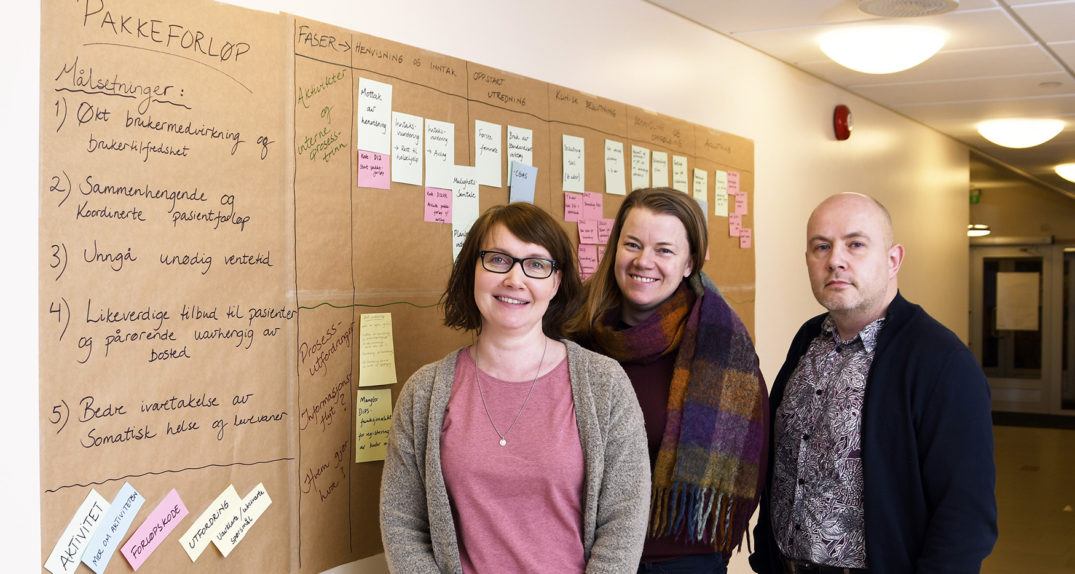 En gruppe mennesker som poserer for et bilde foran en oppslagstavle