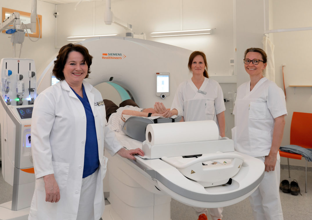 En gruppe kvinner i hvite laboratoriefrakker står ved siden av en pasient