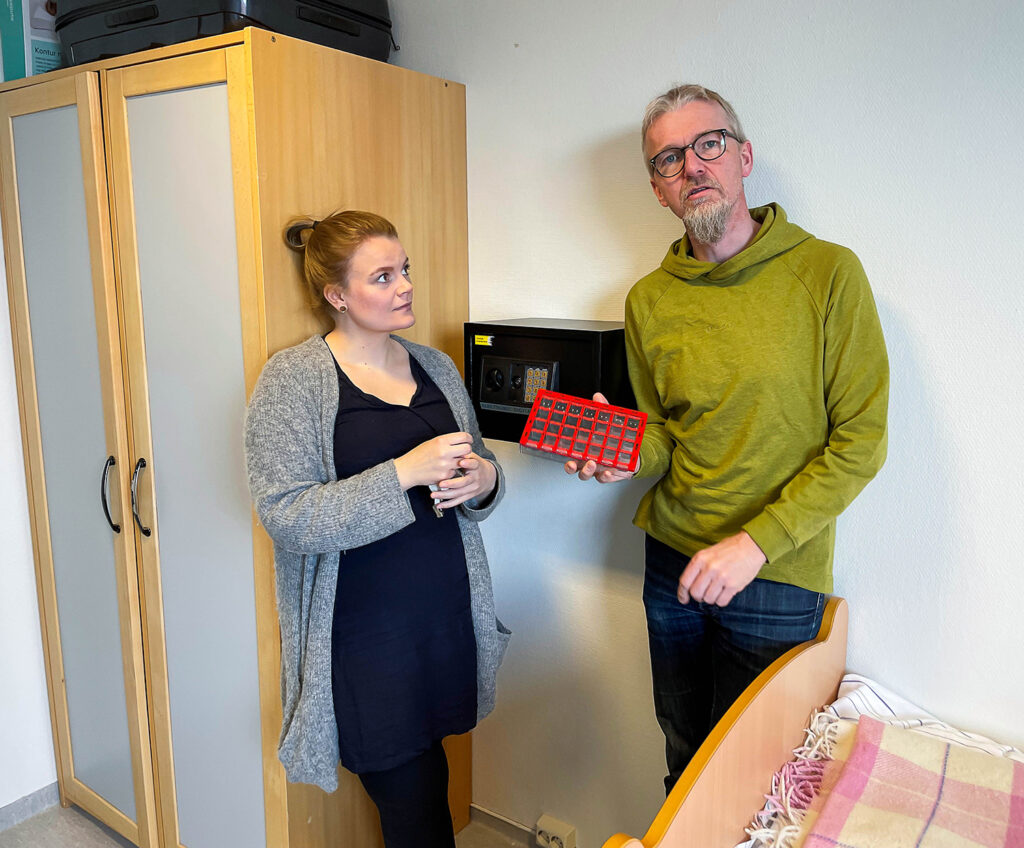To personer på pasientrom viser fram hotellsafe til medisiner