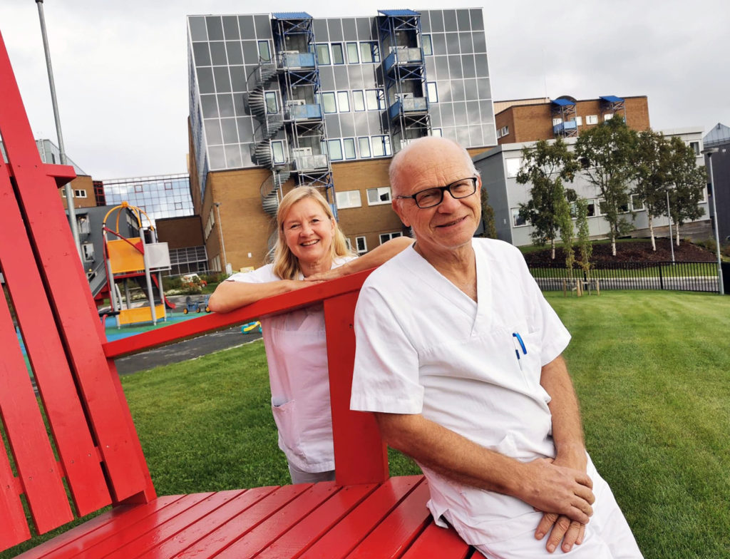 En mann og en kvinne sitter på en rød benk foran en bygning