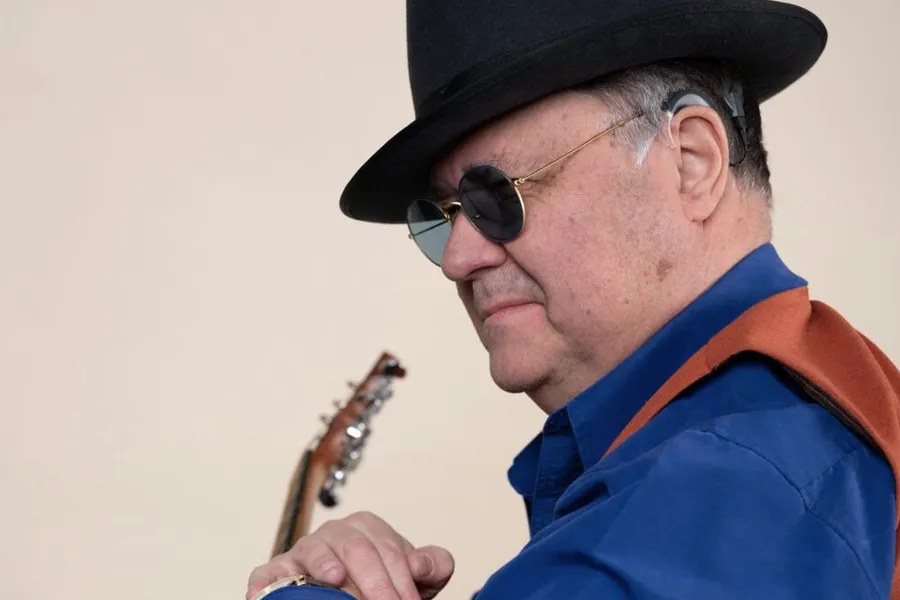 Mann med solbriller og hatt som spiller gitar