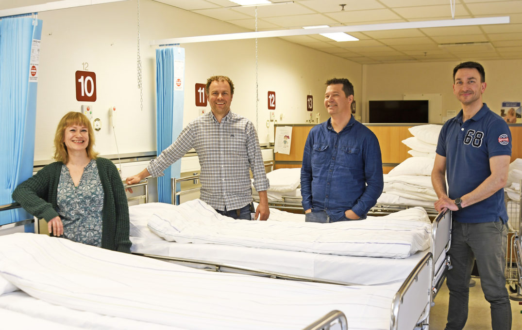 En gruppe mennesker som står ved siden av en seng