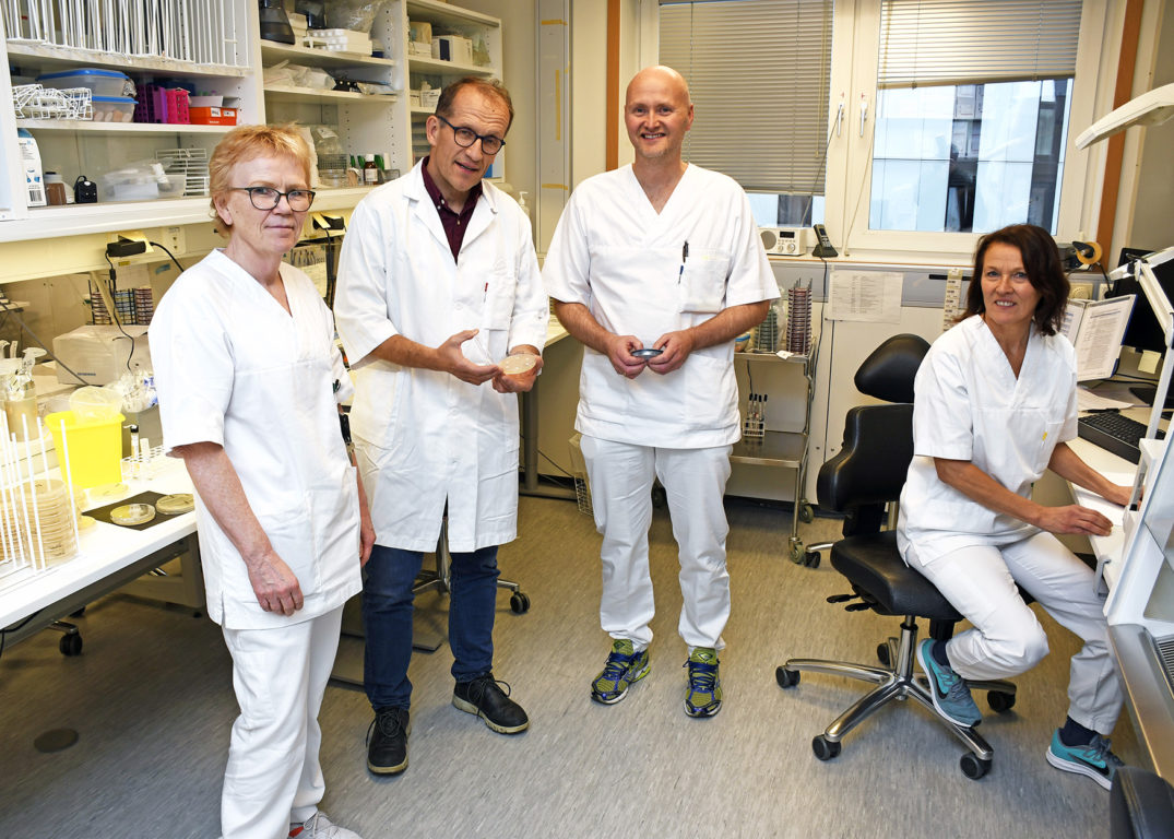 En gruppe mennesker i hvite laboratoriefrakker står i et rom