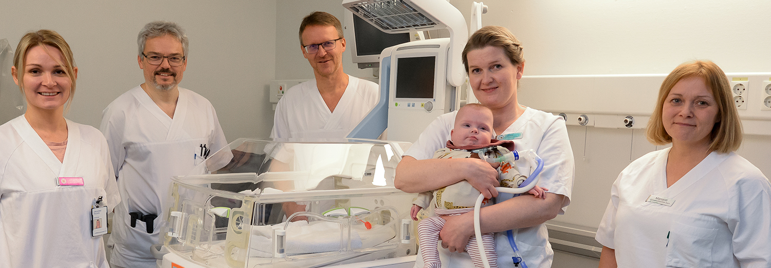 En gruppe mennesker i hvite laboratoriefrakker som holder en baby