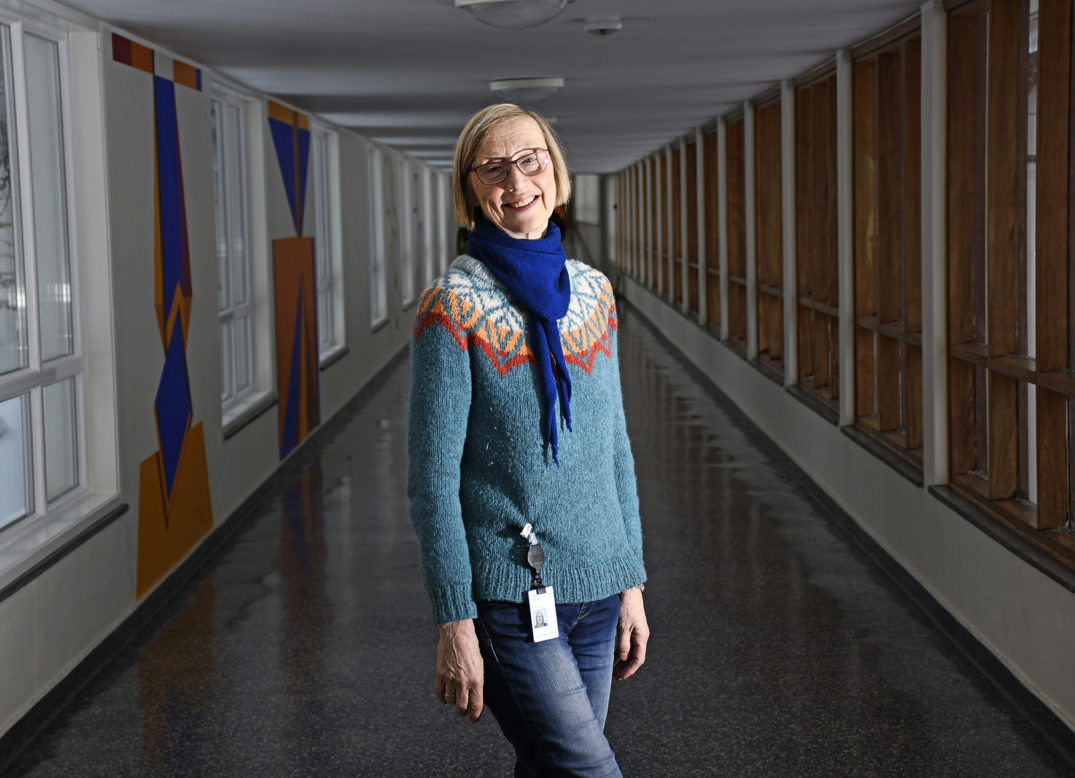 En person med blått skjerf og briller som står i en korridor