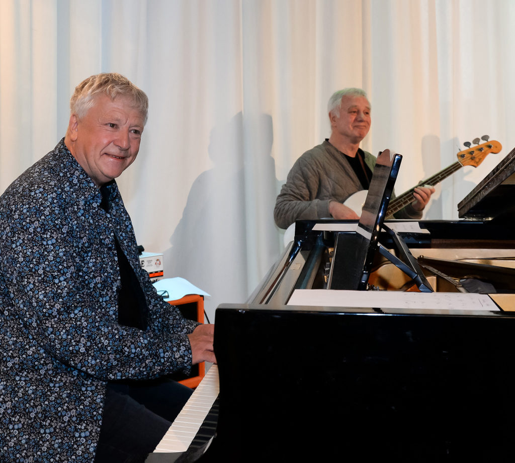 En mann som står ved siden av en mann som sitter ved et skrivebord