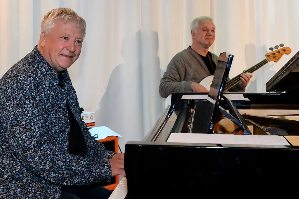 En mann som står ved siden av en mann som sitter ved et skrivebord