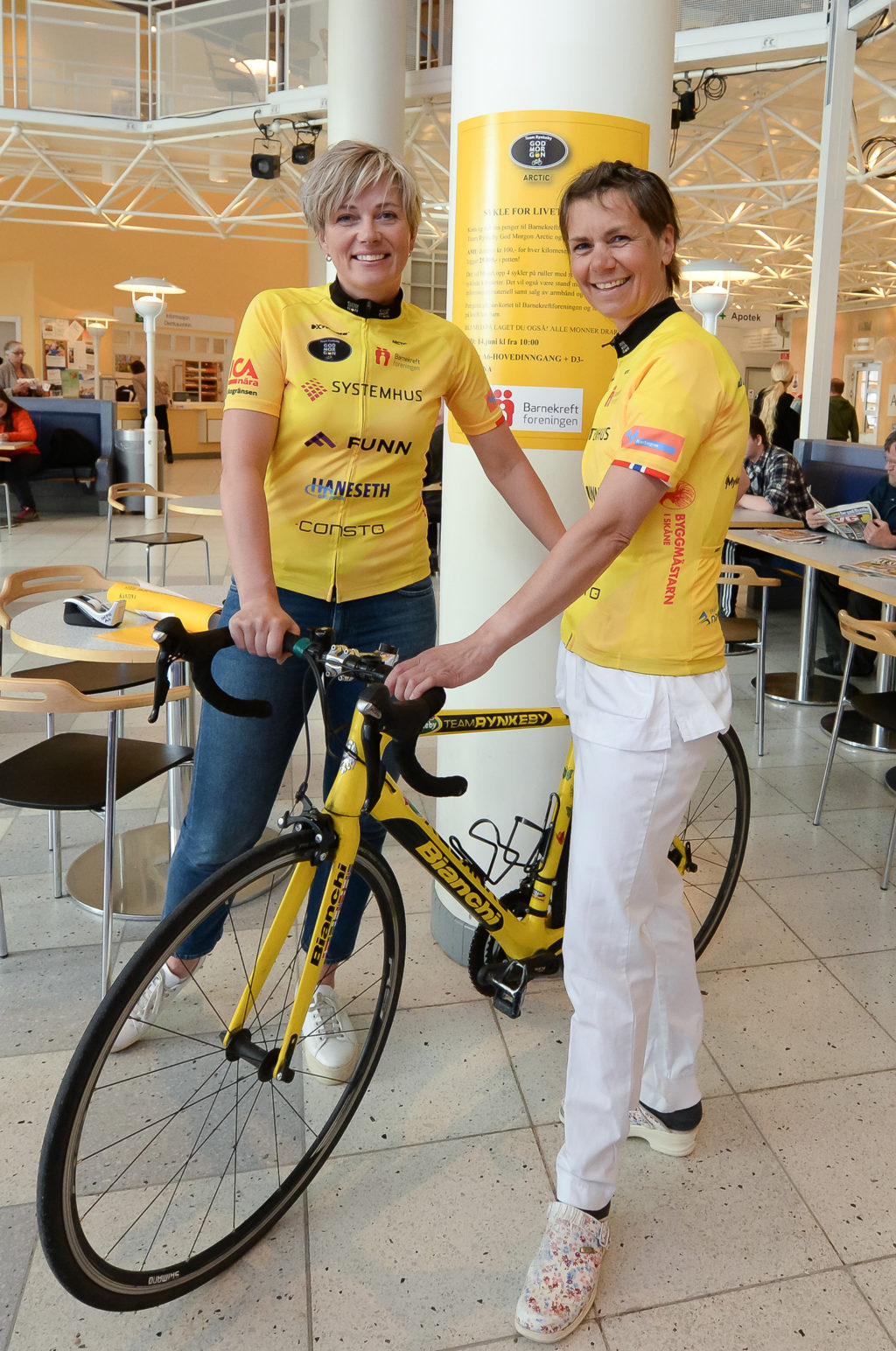 Et par unge menn i gule skjorter som står ved siden av en sykkel