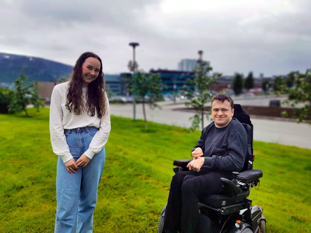 En mann og en kvinne som står ved siden av en rullestol i en park