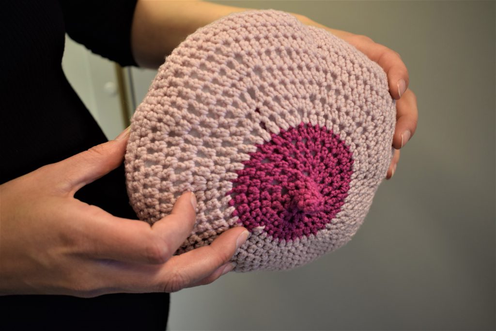 Ved hjelp av denne «strikkepuppen» kan jordmødrene demonstrere hvordan håndmelking utføres. De anbefaler ikke brystpumper, fordi det kun er snakk om de dråpene som enten starter å lekke av seg selv før fødselen, eller som man får ut ved å klemme på brystet.