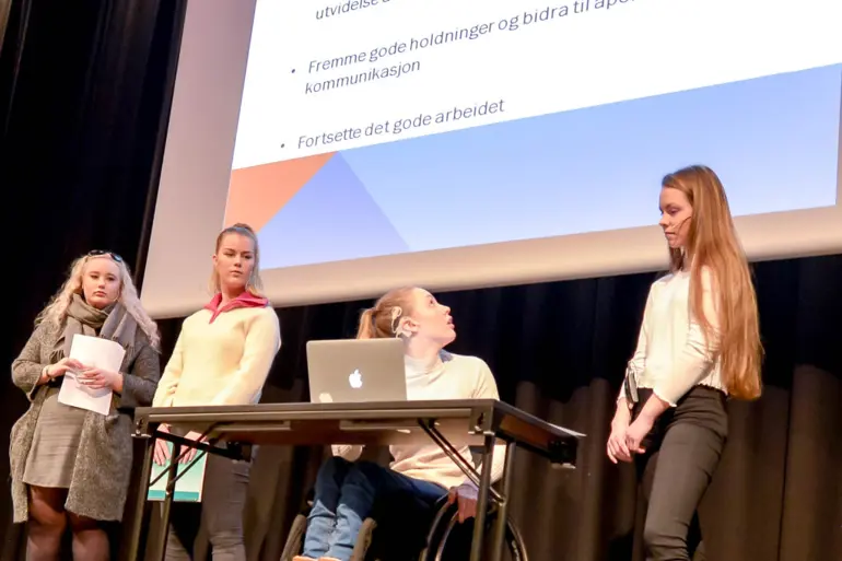 En gruppe mennesker som står rundt en kvinne i rullestol