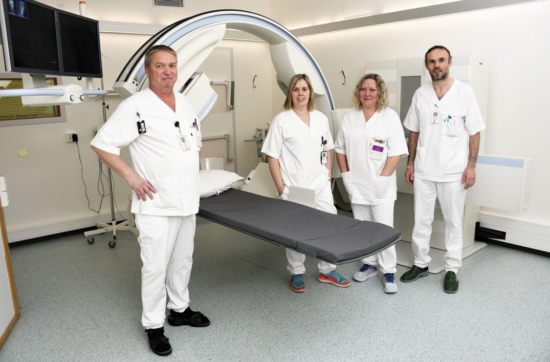 En gruppe mennesker i hvite laboratoriefrakker står foran en seng