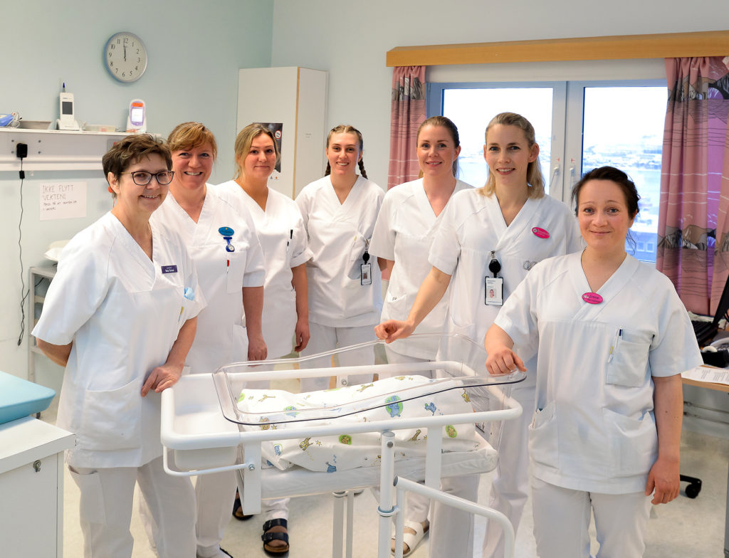 En gruppe kvinner i hvite laboratoriefrakker står ved siden av et bord