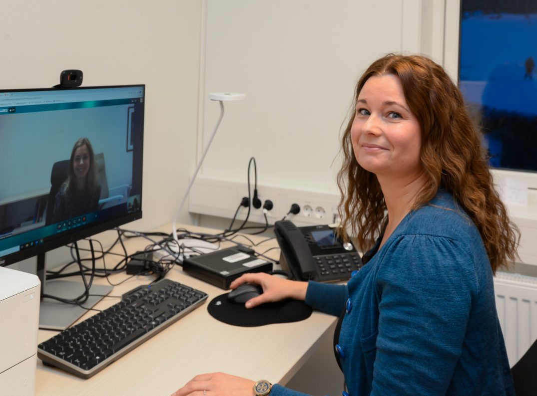 En person som sitter ved et skrivebord med en datamaskin og en telefon