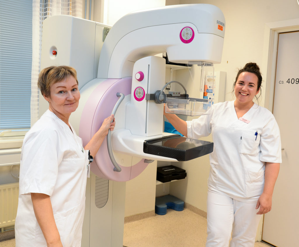 Et par kvinner i hvite laboratoriefrakker som står ved siden av en stor maskin