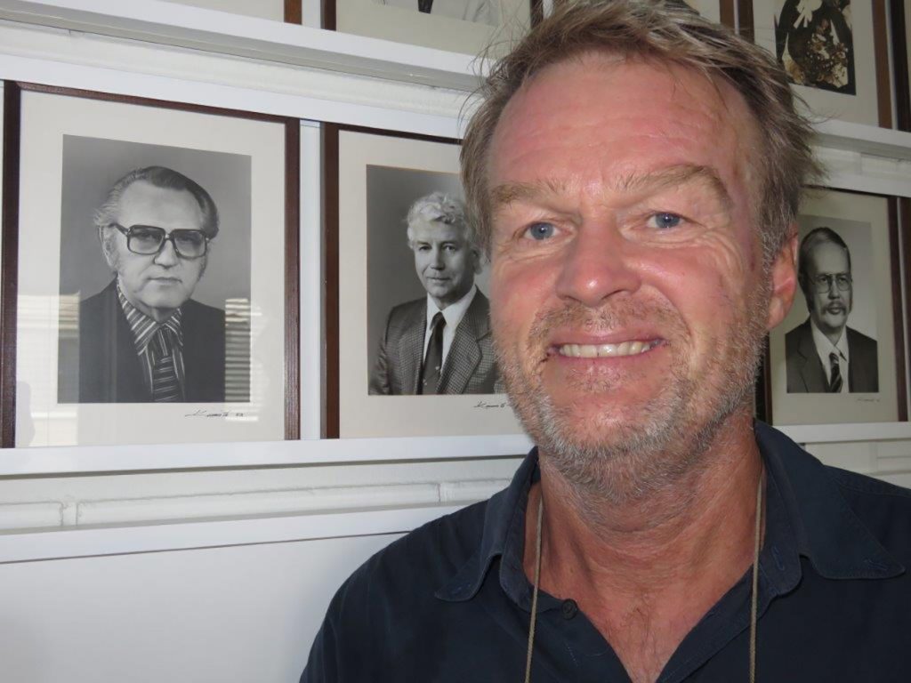 En mann som smiler foran en vegg med bilder