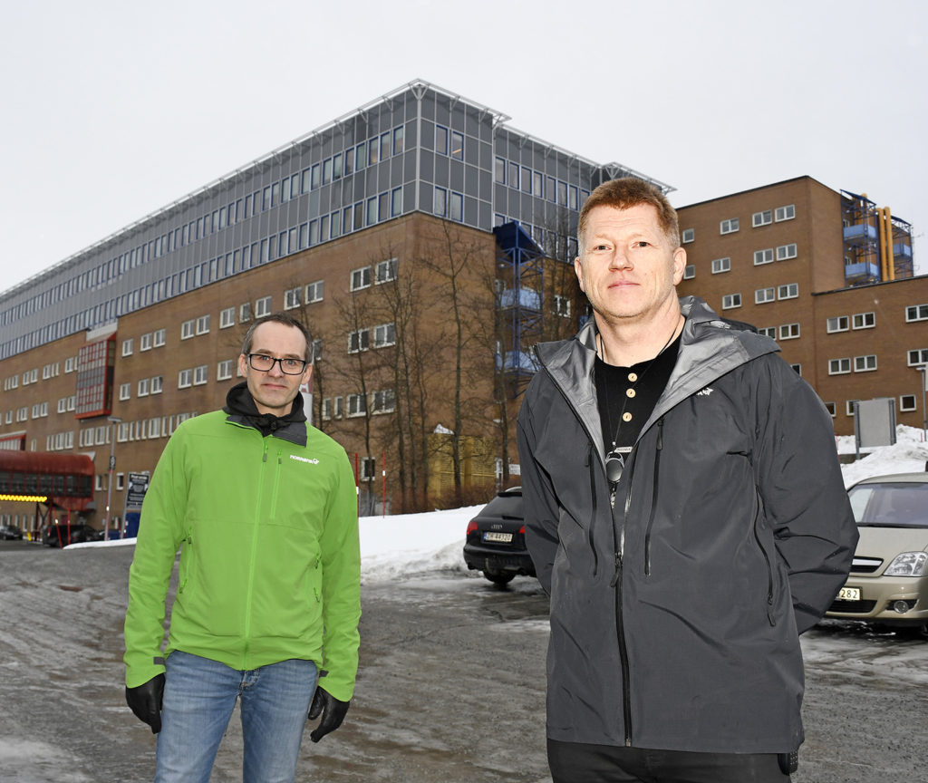 Et par menn som står i snøen foran en bygning