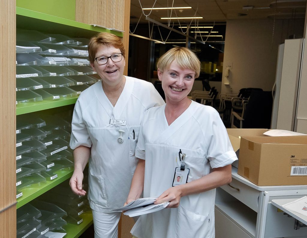 Et par kvinner i hvite laboratoriefrakker som står i et rom med en vannpytt