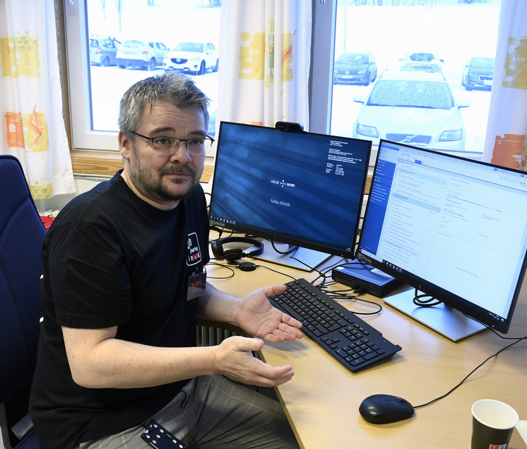 En mann som sitter ved et skrivebord med en datamaskin og et vindu