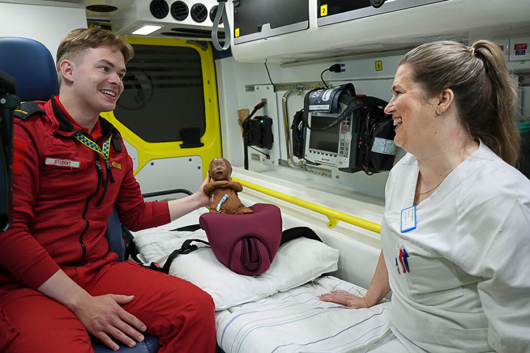 Paramedisiner og jordmor bak i ambulanse, har med simuleringsdukke.