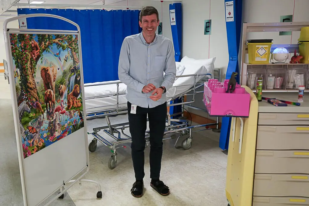 Geir H. Ringvold foran seng og med skillevegg og leker rundt seg