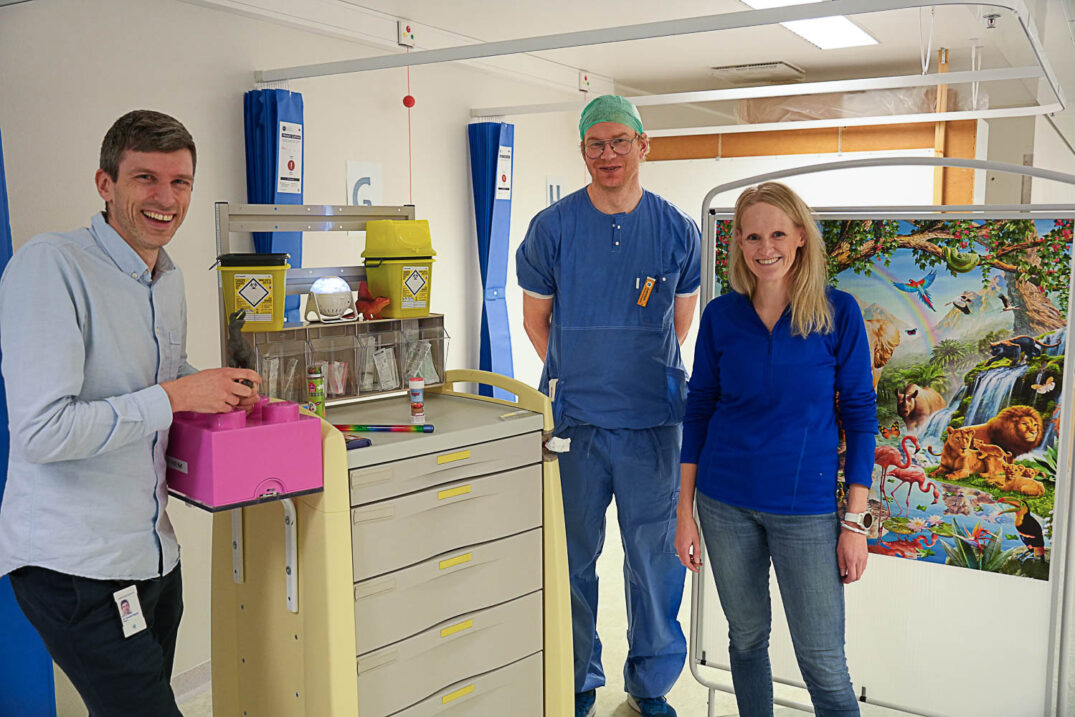 Tre personer poserer foran barnevennlige detaljer i UNN