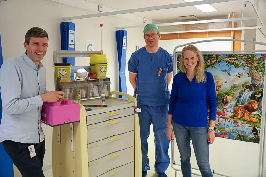 Tre personer poserer foran barnevennlige detaljer i UNN