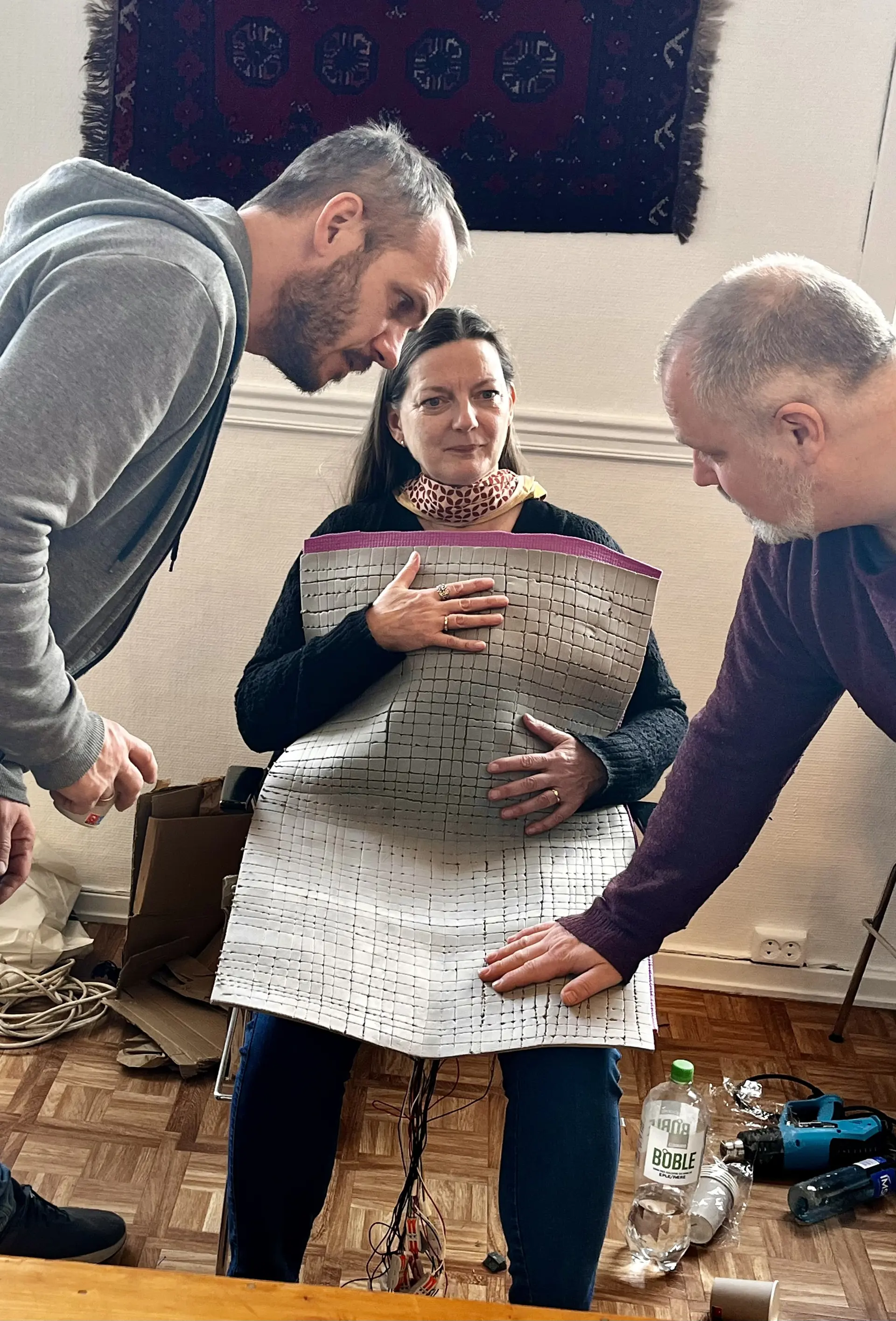 Sittende kvinne med et taktilt teppe over seg. To menn ser på det.