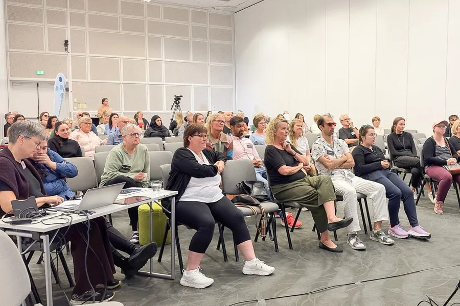 En gruppe mennesker som sitter i et rom. Noen har med seg bærbare datamaskiner