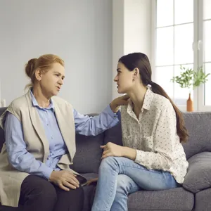 Eldre kvinne snakker med en yngre kvinne. Begge sitter i en sofa.
