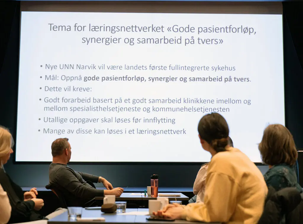 En gruppe mennesker som sitter ved et bord og ser på en skjerm